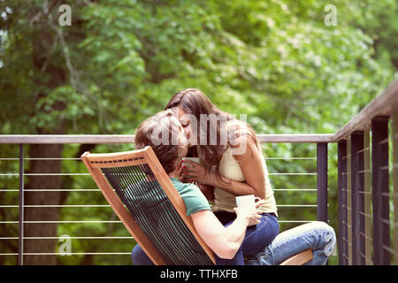Romantic couple kissing while sitting on chair by railing Stock Photo