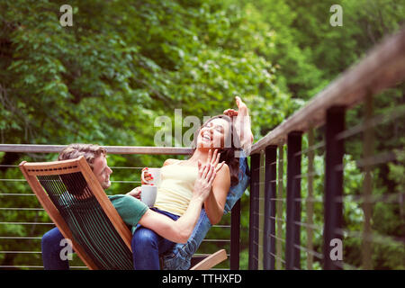 Playful couple laughing while sitting on chair by railing Stock Photo