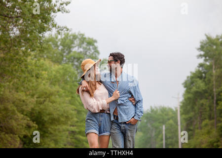 Couple taking while walking by trees against sky Stock Photo