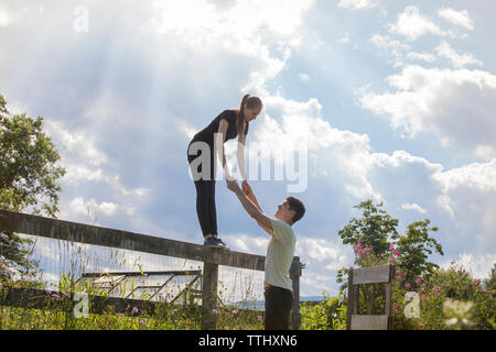 Man holding hands of woman standing on wooden fence in farm Stock Photo