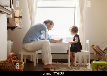 Side view of father teaching daughter coloring at table in home Stock Photo