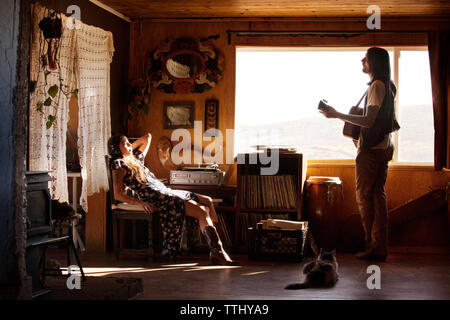 Man playing guitar while woman relaxing on chair at home Stock Photo