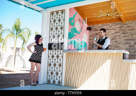 Woman looking at man preparing drink while standing in poolside bar Stock Photo