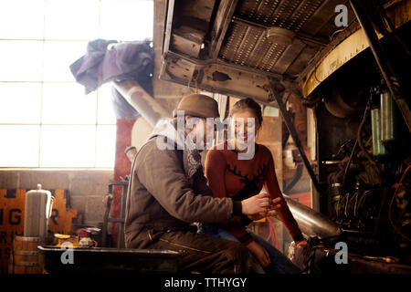 Happy couple sitting by bus in auto repair shop Stock Photo