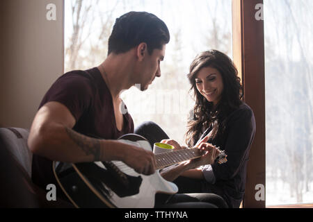 Man playing guitar while woman sitting on window sill Stock Photo