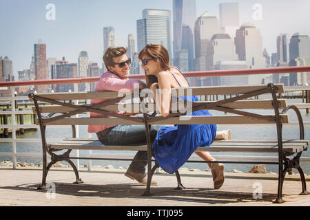 Happy couple sitting on bench by railing Stock Photo