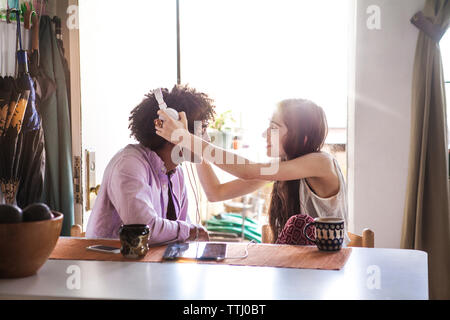 Woman assisting man in wearing headphone at table in home Stock Photo