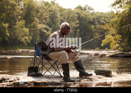 Person sitting at side of lake fishing with rod England Stock Photo - Alamy
