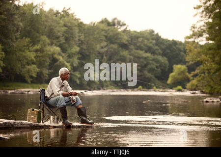 Man fishing while sitting on chair at lake Stock Photo