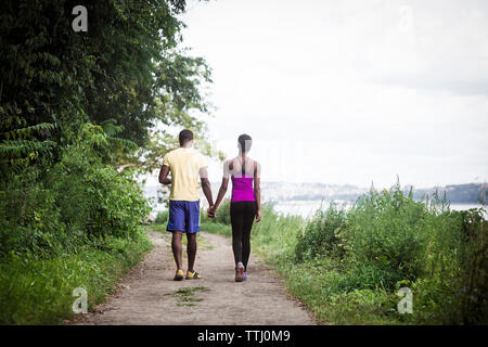 Rear view of couple holding hands while walking on road amidst grass Stock Photo