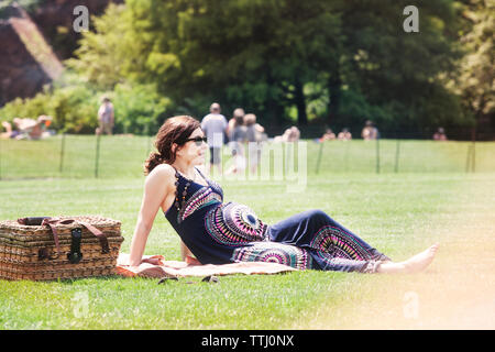 Pregnant woman sitting on grassy field in park Stock Photo