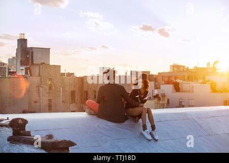 Happy couple sitting on retaining wall against buildings Stock Photo