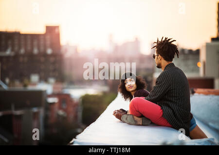 Woman looking at man sitting on retaining wall during sunset Stock Photo