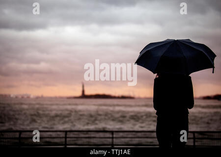 Rear view of woman with umbrella standing against cloudy sky Stock Photo