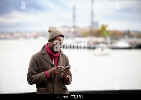 Smiling man using mobile phone while standing by railing against sea Stock Photo