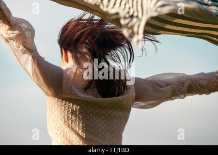 Low angle view of woman holding aloft scarf against sky Stock Photo