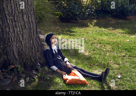 Girl in costume sitting by tree trunk in lawn Stock Photo