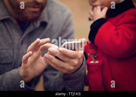Midsection of father with baby girl using smart phone in park Stock Photo