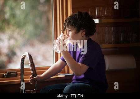 Boy drinking water while sitting at kitchen counter in home Stock Photo