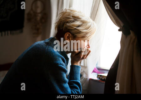 Woman with hand on chin looking away though window at home Stock Photo