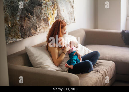 Mother feeding baby girl while sitting on sofa at home Stock Photo