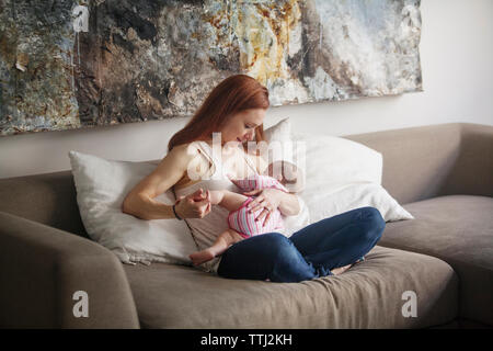 Happy mother feeding baby girl while sitting on sofa at home Stock Photo