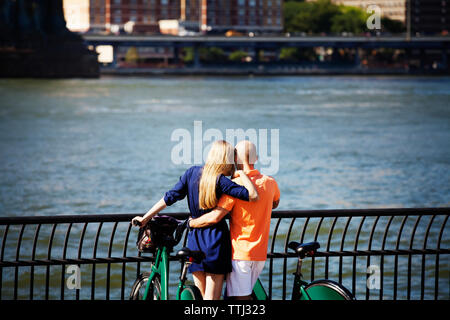 Rear view of couple with bicycles standing against east river Stock Photo