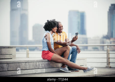 Smiling couple taking selfie while sitting on steps at promenade Stock Photo