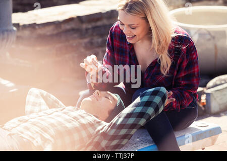 Smiling woman holding dry leaf while man lying on bench Stock Photo