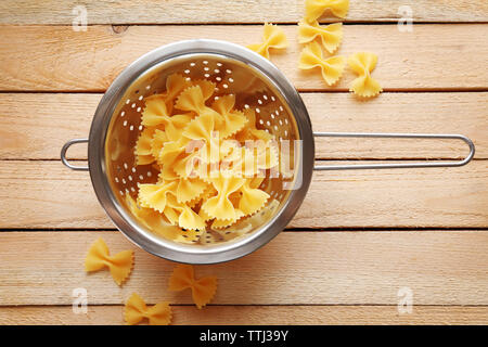 Pasta farfalle in  drainer on wooden table background Stock Photo