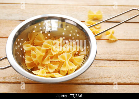 Pasta farfalle in  drainer on wooden table background Stock Photo
