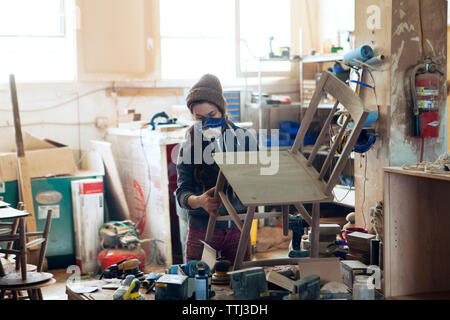 Female carpenter examining wooden chair in workshop Stock Photo