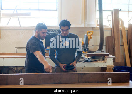 Male carpenters discussing over wooden plank at workshop Stock Photo