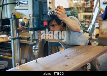 Male carpenter using machinery on wooden plank at workshop Stock Photo