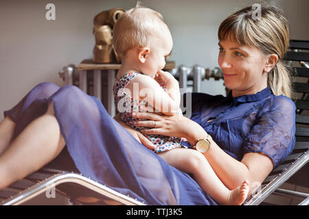 Mother playing with baby while sitting on lounge chair at home Stock Photo