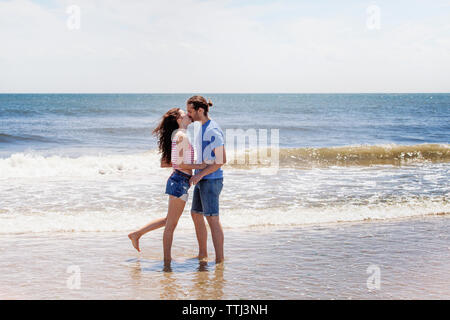 Affectionate couple kissing while standing on shore at beach Stock Photo