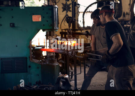 Blacksmiths forging rod in machinery at workshop Stock Photo