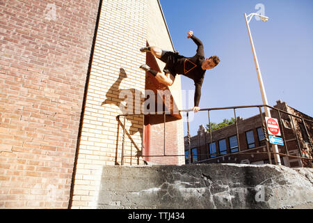 Low angle view of confident man jumping over railing against clear blue sky Stock Photo