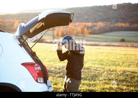 Side view of man wearing headlamp while standing by car on field Stock Photo