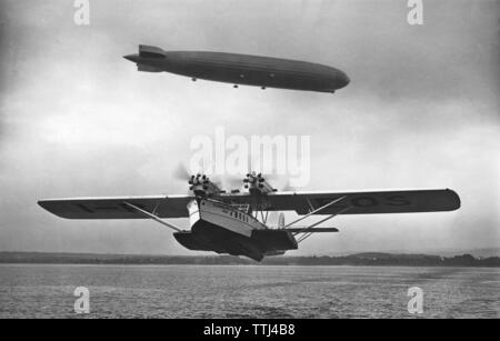 Aviation history. Airship Graf Zeppelin LZ 127 airborn with the amphibian aircraft Dornier Superwal starting in front. 1930s Stock Photo