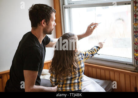 Father and son drawing on window glass while kneeling on bed at home Stock Photo