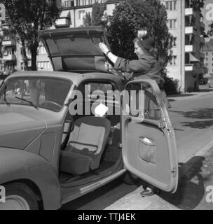 Driving in the 1950s. A young woman in her Fiat convertible car. Note the car door that opens forward and there are no seatbelts. It´s a warm and sunny day and the roof top is removed. Her daughter is seen in the car. Sweden 1951. ref 1711 Stock Photo