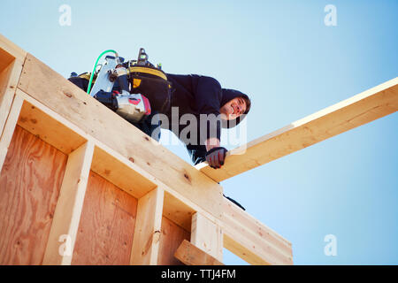 Low angle view of smiling worker making construction frame against clear blue sky Stock Photo