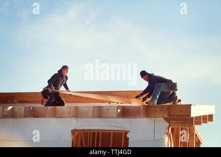 workers constructing roof beam against sky during sunny day Stock Photo