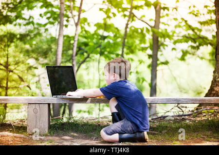 Side view of boy using laptop computer at concrete bench Stock Photo