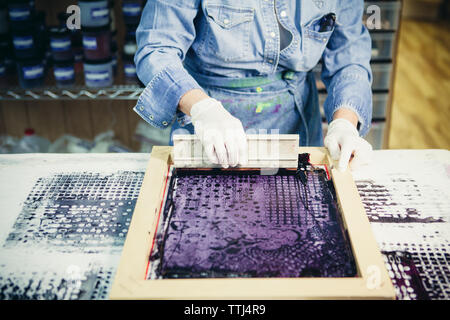 Midsection of craftswoman using silk screen to print design on fabric at workshop Stock Photo