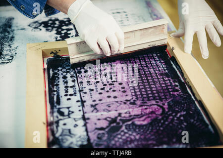 Cropped hands of craftswoman using silk screen to print design on fabric at workshop Stock Photo