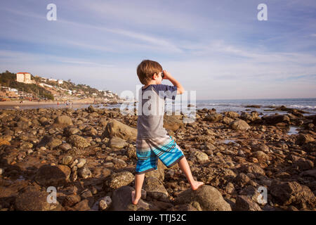 Boy looking through binoculars at beach Stock Photo