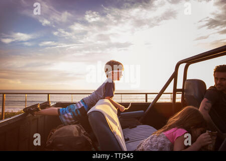 Family in pick-up truck by sea during sunset Stock Photo