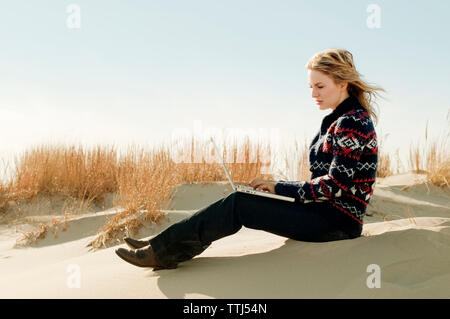 Woman using laptop computer while sitting on sand Stock Photo